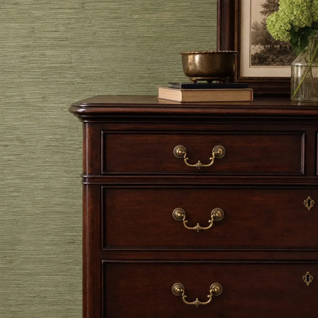 Close up of a rich mahogany dresser set against a sage green textured grasscloth wall
