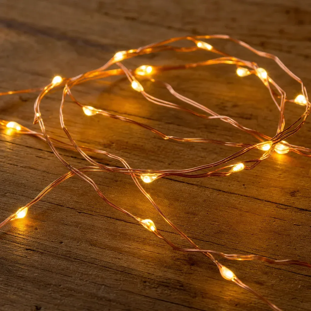 Close up of flexible copper wire LED fairy lights resting on a wooden table