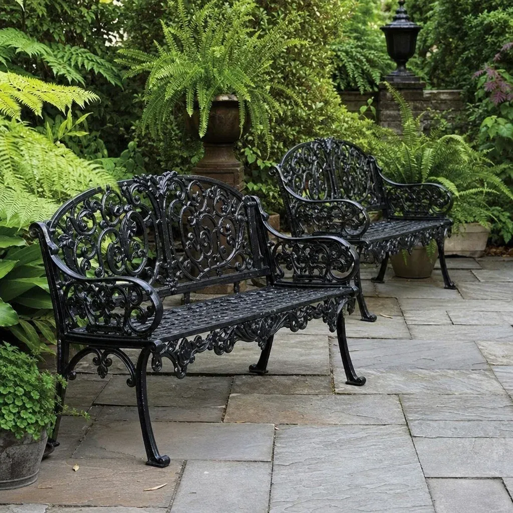 Victorian wrought iron garden benches placed neatly on a stone patio surrounded by ferns