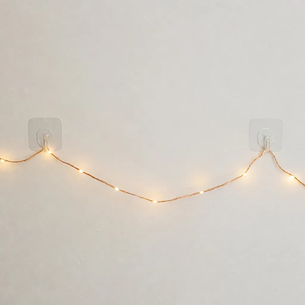 Clear adhesive hooks holding up a thin strand of copper fairy lights on a white wall